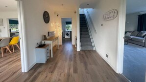 A modern living space with a staircase leading to a second floor, a dining area with a table and chairs, and a laundry room. - Luxury 5-bed House With Tennis Court & Games Room (Steyning)