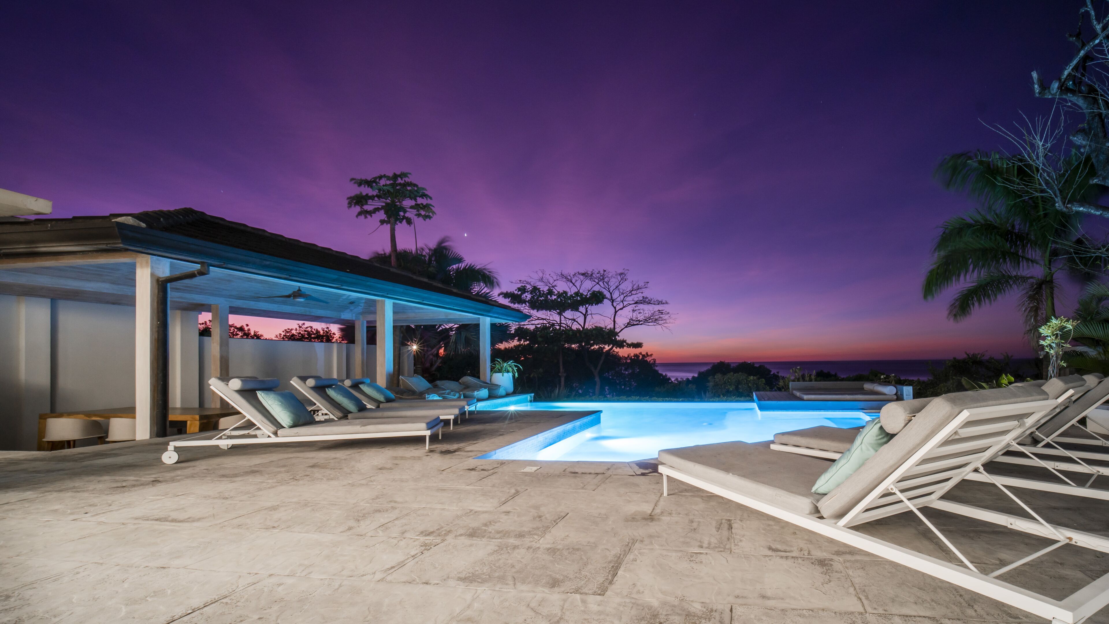 A pool area with lounge chairs and a covered seating area, overlooking a scenic view.