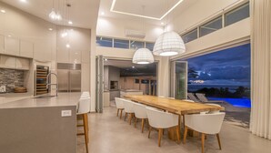 Eine moderne Küche mit Kochinsel, Edelstahlgeräten und einem Essbereich mit Holztisch und weißen Stühlen.