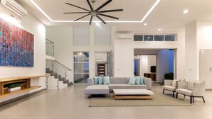 Ein großzügiger Wohnraum mit Ecksofa, Couchtisch und Kamin. Eine Treppe führt auf eine obere Ebene, und ein großes Fenster sorgt für natürliches Licht.