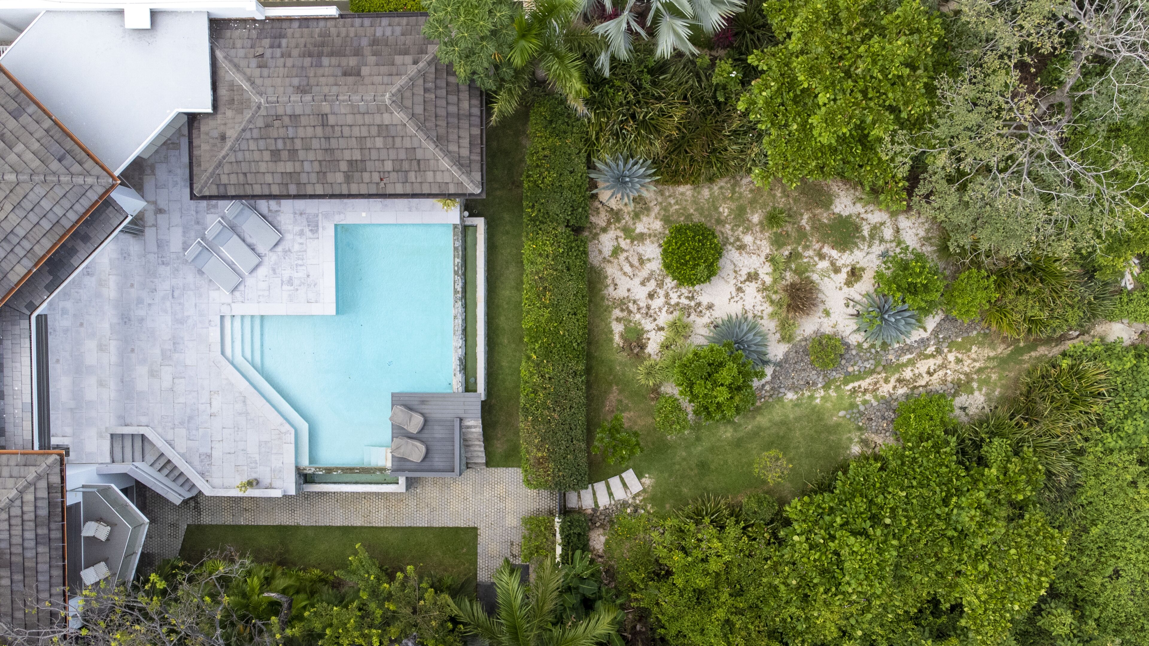 Luchtbeeld van een modern huis met een zwembad, een terras en een aangelegde tuin.