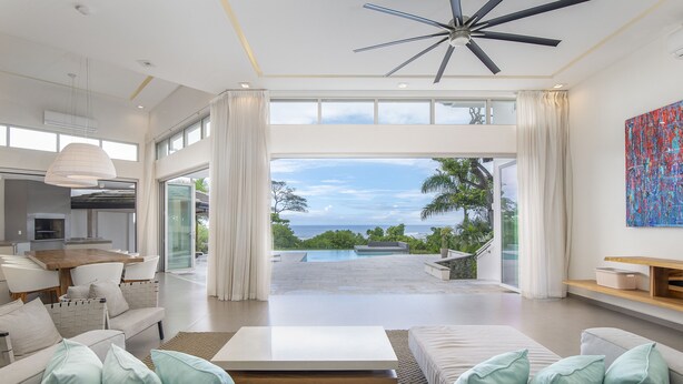 Ein geräumiges Wohnzimmer mit einer großen Couch, einem Couchtisch und Blick auf einen Swimmingpool und den Ozean.