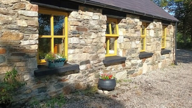 Un edificio de piedra con tres ventanas, cada una con marcos amarillos y una maceta pequeña con flores.