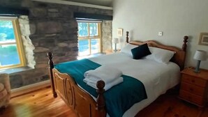 Un dormitorio con cama de madera, pared de piedra y una ventana.
