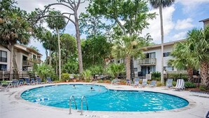 Una piscina rodeada de sillas de descanso y palmeras, con un edificio al fondo.
