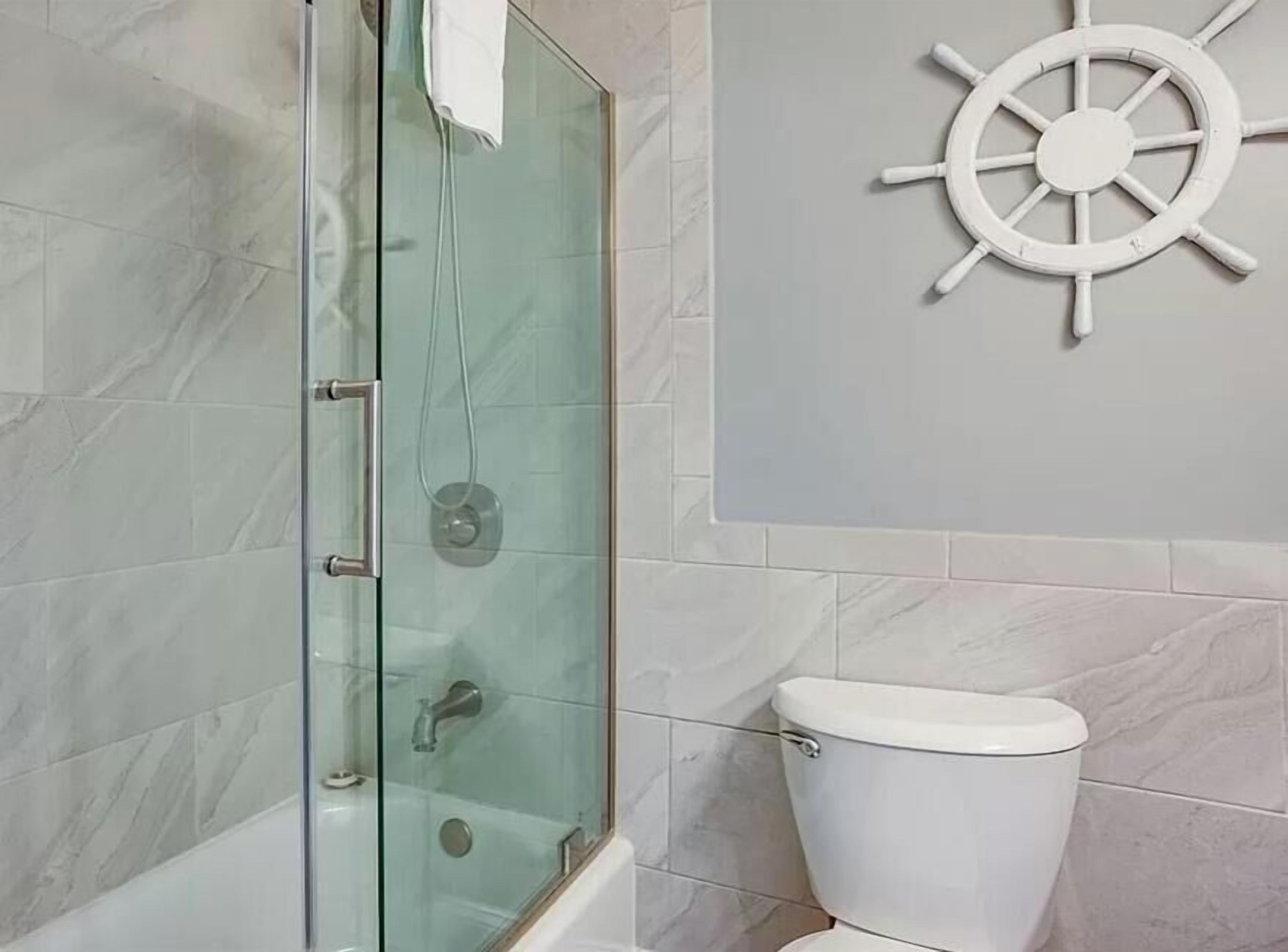 Une salle de bain avec une douche à parois de verre, des toilettes blanches et une décoration murale représentant un gouvernail de bateau.