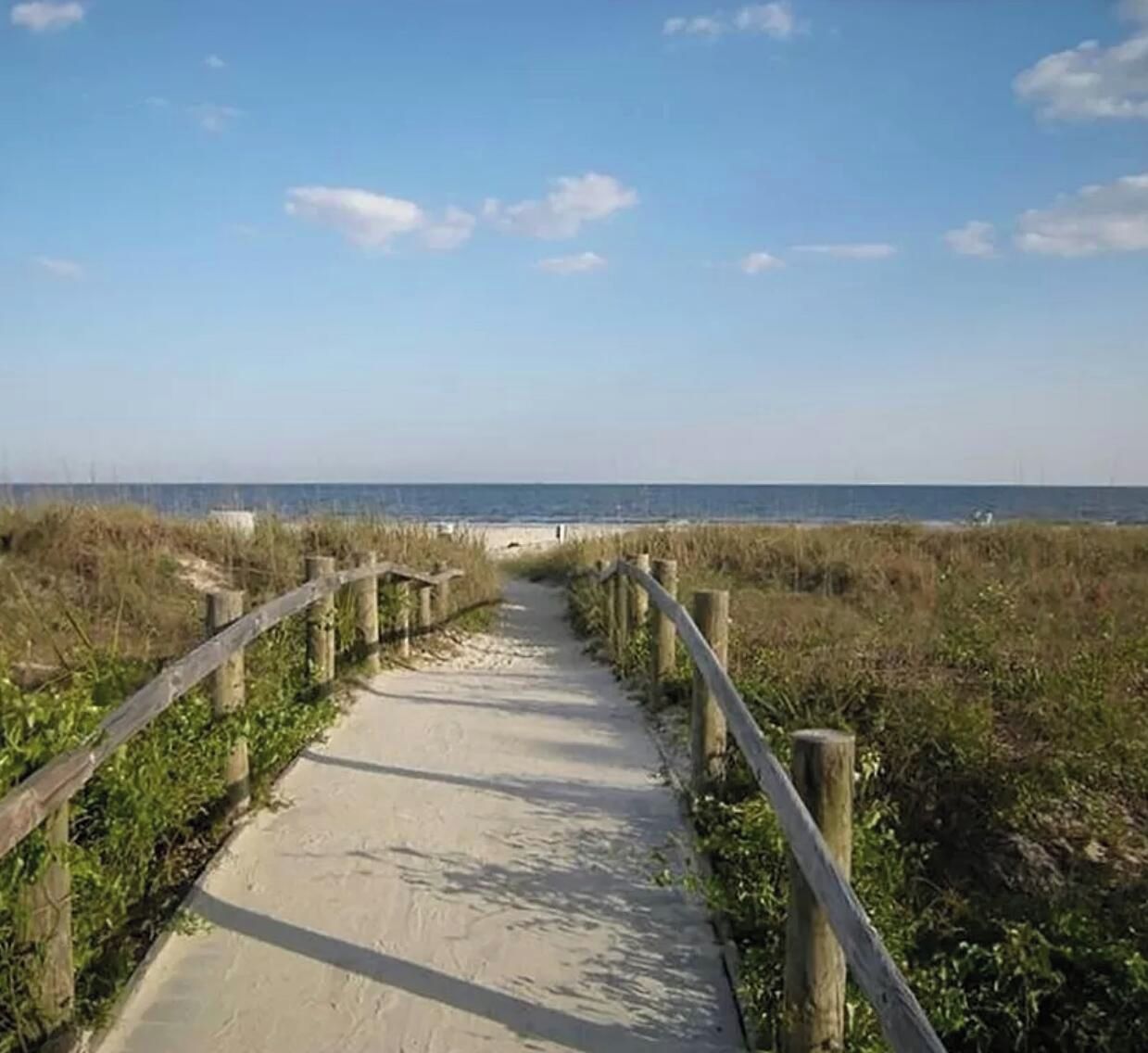 A concrete pathway flanked by wooden posts leading to a beach.