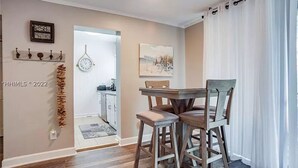 Un comedor con una mesa y sillas de madera, un reloj en la pared y una cocina al fondo.