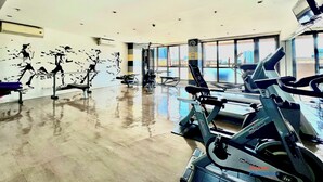 Una palestra con diverse attrezzature, ampie finestre e vista sulla città.