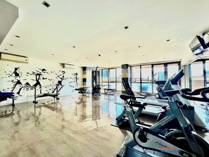 A gym with various exercise equipment, large windows, and a view of the cityscape. -  KL Tower - Clean & Cozy 1BR Unit near Greenbelt Mall Makati City (Makati)