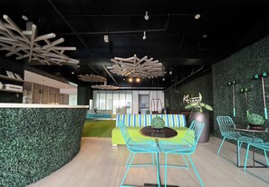 Ein modernes Interieur mit einer Rezeption, einem grünen Sofa und blauen Stühlen um einem kleinen Tisch.