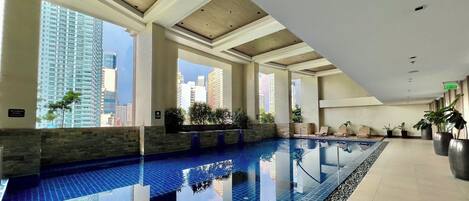 Una piscina interior con baldosas azules brillantes, ventanas amplias y vistas de edificios circundantes.