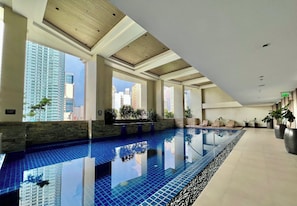 An indoor swimming pool with clear blue tiles, large windows, and a view of surrounding buildings.