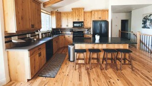 Una cocina amplia con armarios de madera, una isla central con taburetes, un lavaplatos de acero inoxidable y un refrigerador negro.