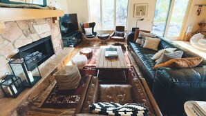 Una sala de estar acogedora con chimenea de piedra, sofá de cuero y un amplio ventanal.
