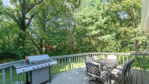 A deck with a grill, table, and chairs, surrounded by trees. - Amazing Escape - 4 BEDS, 3 BEDROOMS, Private Deck near DC (Annandale)