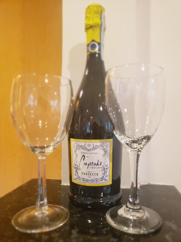 A bottle of Prosecco wine with a label from Cupcake Vineyards, placed between two empty wine glasses on a black surface. - Amazing Escape - 4 BEDS, 3 BEDROOMS, Private Deck near DC (Annandale)