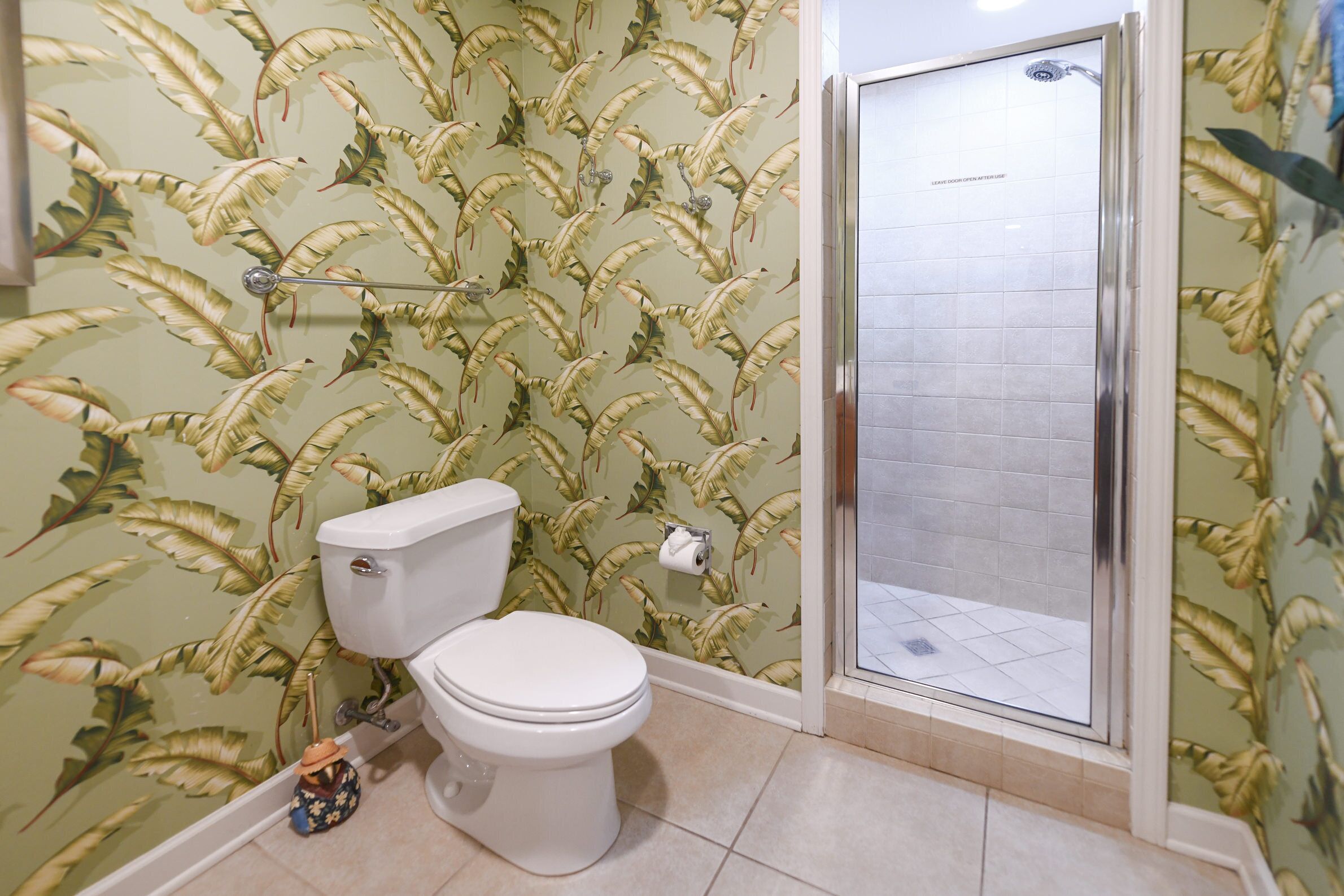 A bathroom with a toilet, shower, and patterned wallpaper.
