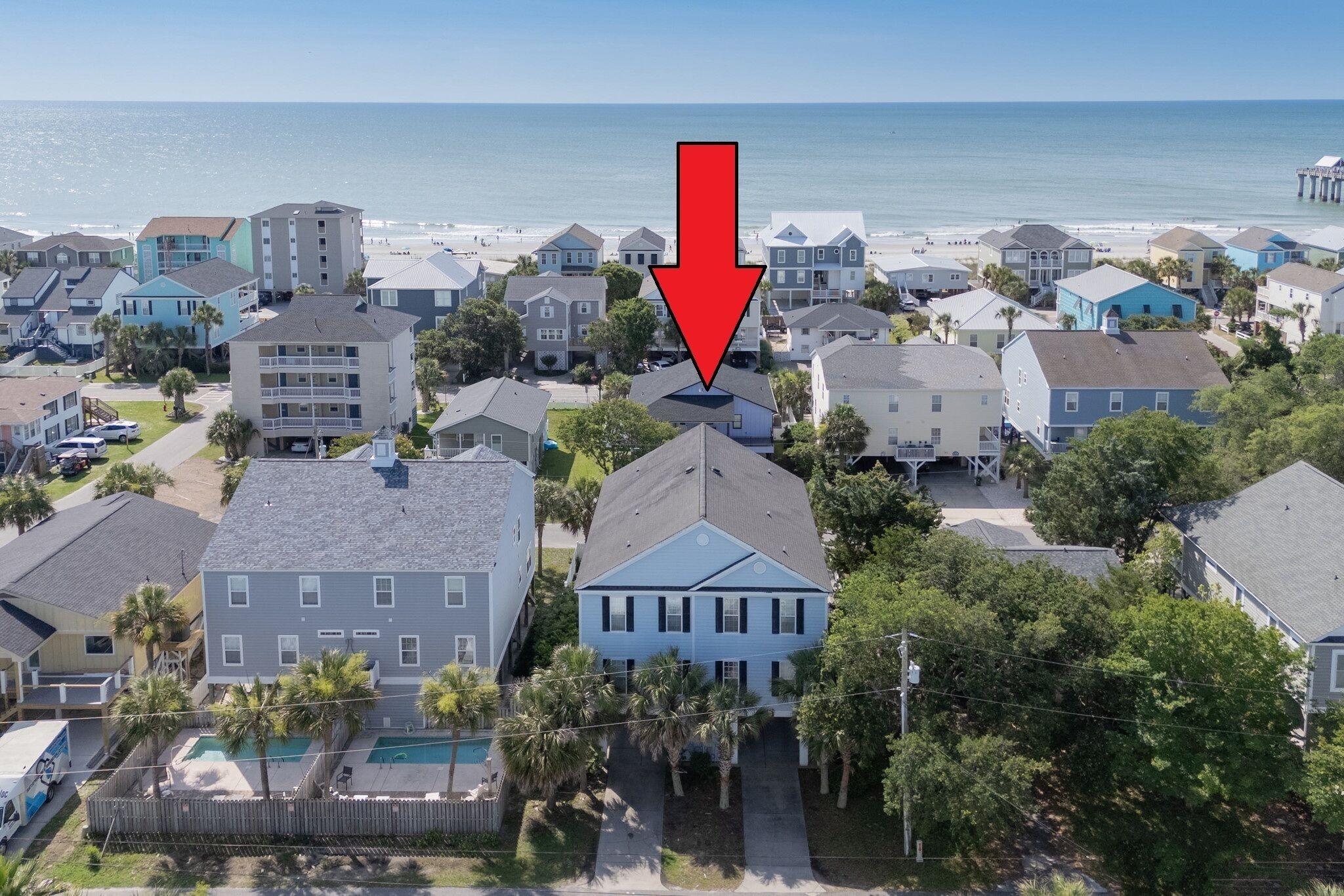 Una zona residencial costera con casas, una playa y un muelle al fondo.