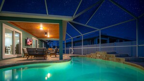 A swimming pool with a covered area, lounge chairs, and a television screen. - Private Heated Pool | 5 Min to Beach | Bikes + Fire Pit (Marco Island)