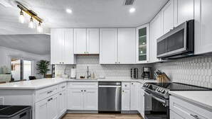 A modern kitchen with white cabinets, a stainless steel dishwasher, a built-in oven, and a microwave. - Private Heated Pool | 5 Min to Beach | Bikes + Fire Pit (Marco Island)