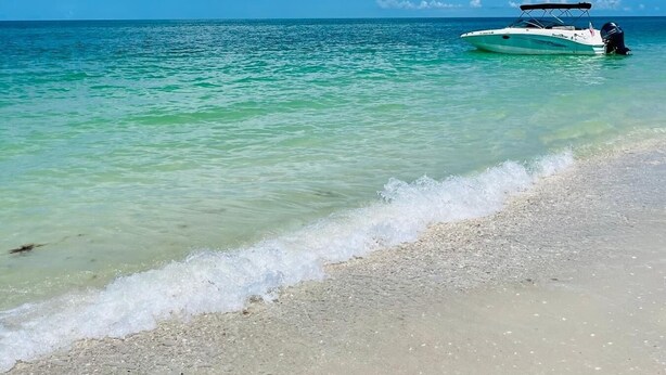 A beach with clear turquoise water, a boat in the distance, and a clear blue sky. - Private Heated Pool | 5 Min to Beach | Bikes + Fire Pit (Marco Island)