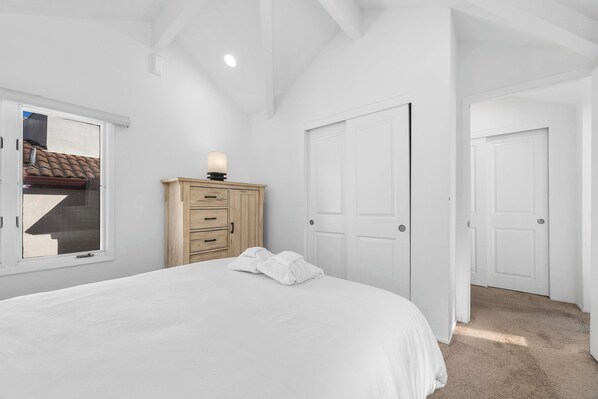 A bedroom with a bed, a wooden dresser, a window, and a door.