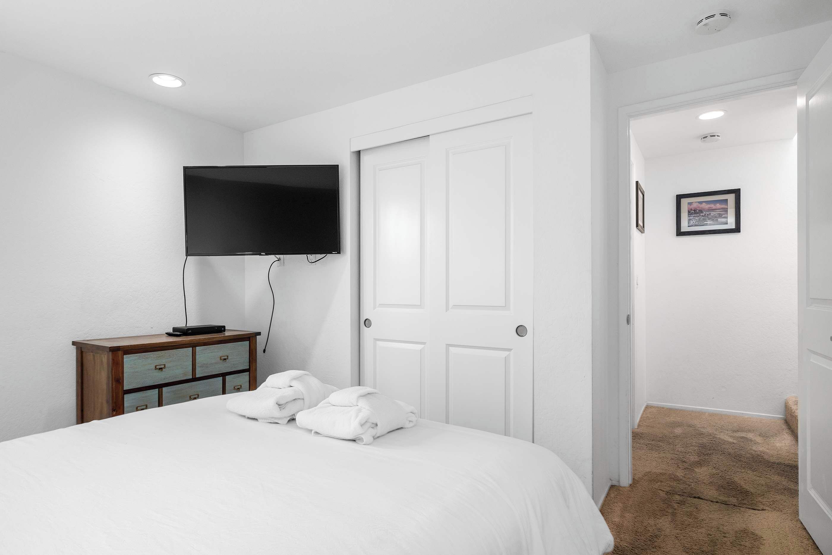 Een hotelkamer met een bed, een flatscreen televisie aan de muur, een houten dressoir en een deur die naar een andere kamer leidt.