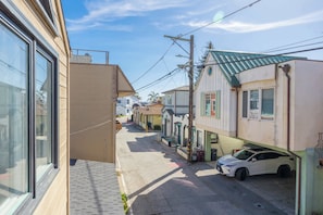 Une rue étroite bordée d’immeubles d’habitation, avec une voiture garée et des poteaux électriques visibles.