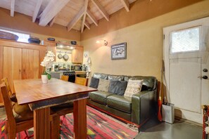 Uma sala de estar aconchegante com uma mesa de jantar de madeira, um sofá de couro e uma cozinha ao fundo.