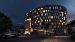 Un hôtel moderne à la façade incurvée, doté de nombreux balcons et d’une entrée bien éclairée.