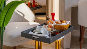 Une chambre d’hôtel avec un lit, une table de chevet ornée d’un vase de fleurs, un plateau avec des articles pour le petit-déjeuner et une plante en pot.
