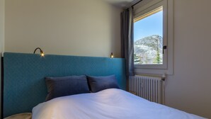 Une chambre à coucher avec un lit, une tête de lit, une fenêtre avec des rideaux et un radiateur.