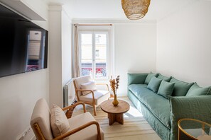 A living room with a green sofa, a wooden coffee table with a vase, a beige armchair, and a television mounted on the wall. - Eiffel Tower Rue Cler (Paris)