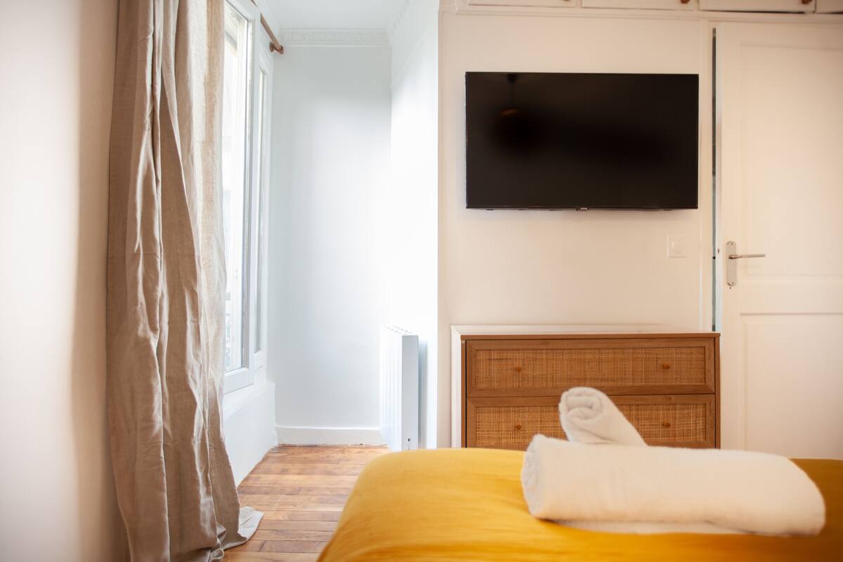 Habitación de hotel con una cama, un televisor montado en la pared y una ventana con cortinas.