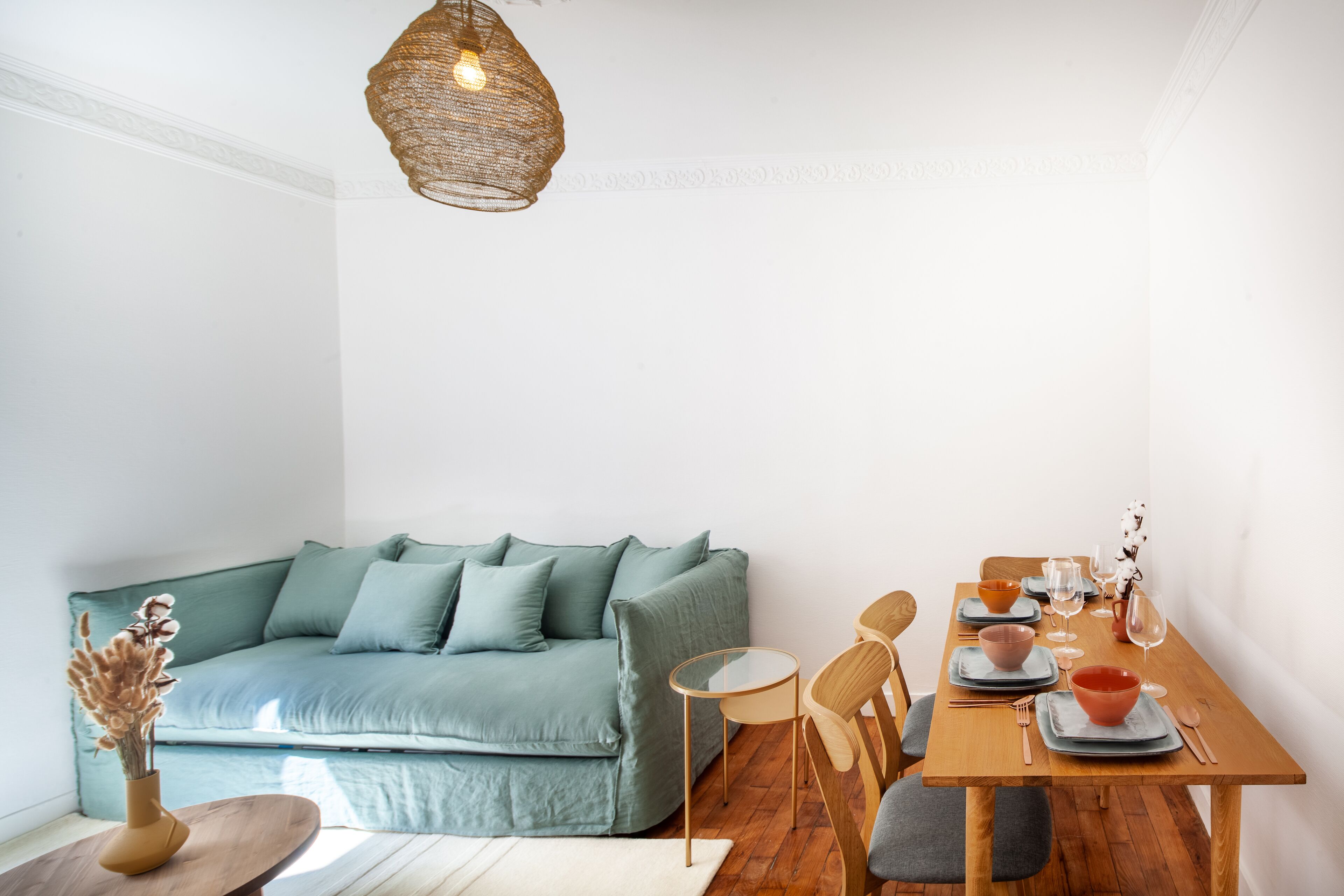 Un salon moderne avec un canapé de couleur turquoise, une table à manger en bois et un luminaire suspendu.