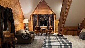 A cozy attic bedroom with a loft bed, a small dining table, a sofa, and a lamp. - Lodge Suites at Susitna River Lodge (Talkeetna)