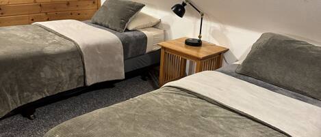 A bedroom with two single beds, a wooden headboard, a small bedside table with a lamp, and a carpeted floor.