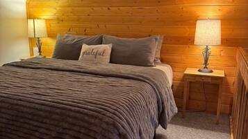 Ein gemütliches Schlafzimmer mit schrägverlegtem Holzboden, einem Bett mit einer strukturierten Decke, zwei Nachttischlampen und einem Kissen mit dem Wort 'grateful'.