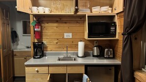 A compact kitchen with wooden cabinetry, a built-in microwave, a coffee maker, and a sink. - Lodge Suites at Susitna River Lodge (Talkeetna)