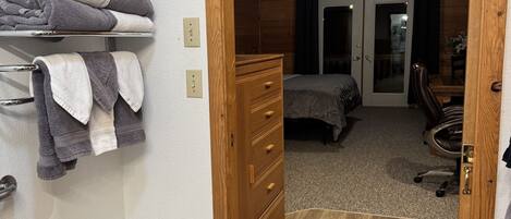 A room with a wooden wardrobe, a small white stool, a bed, and a bench.