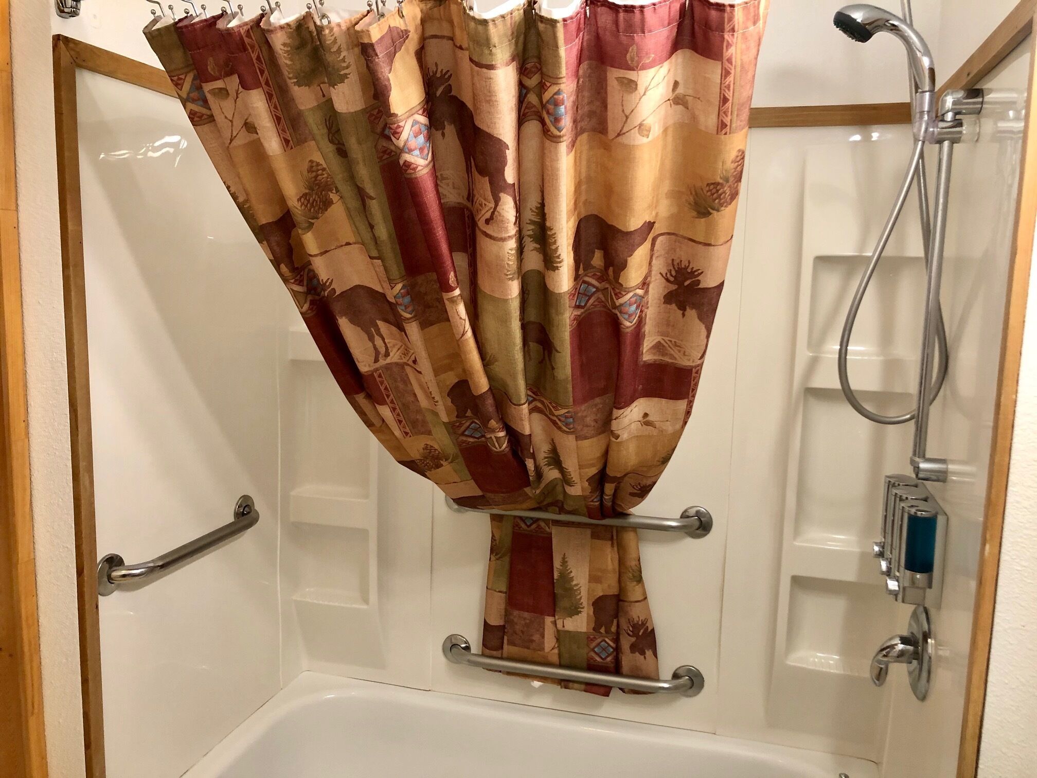 A bathroom with a shower curtain featuring a nature pattern, a handheld showerhead, and a grab bar.