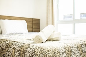 Uma cama bem arrumada com um edredom estampado, uma toalha enrolada e um travesseiro.