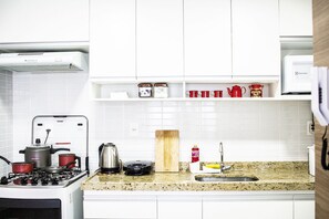 Uma cozinha com armários brancos, fogão a gás, micro-ondas e diversos utensílios sobre o balcão.