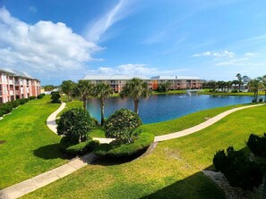 A well-maintained hotel courtyard with a central water feature, surrounded by neatly trimmed grass and palm trees.