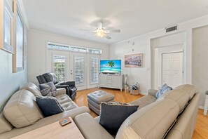 A spacious living room with a ceiling fan, a television, and a large window with blinds.