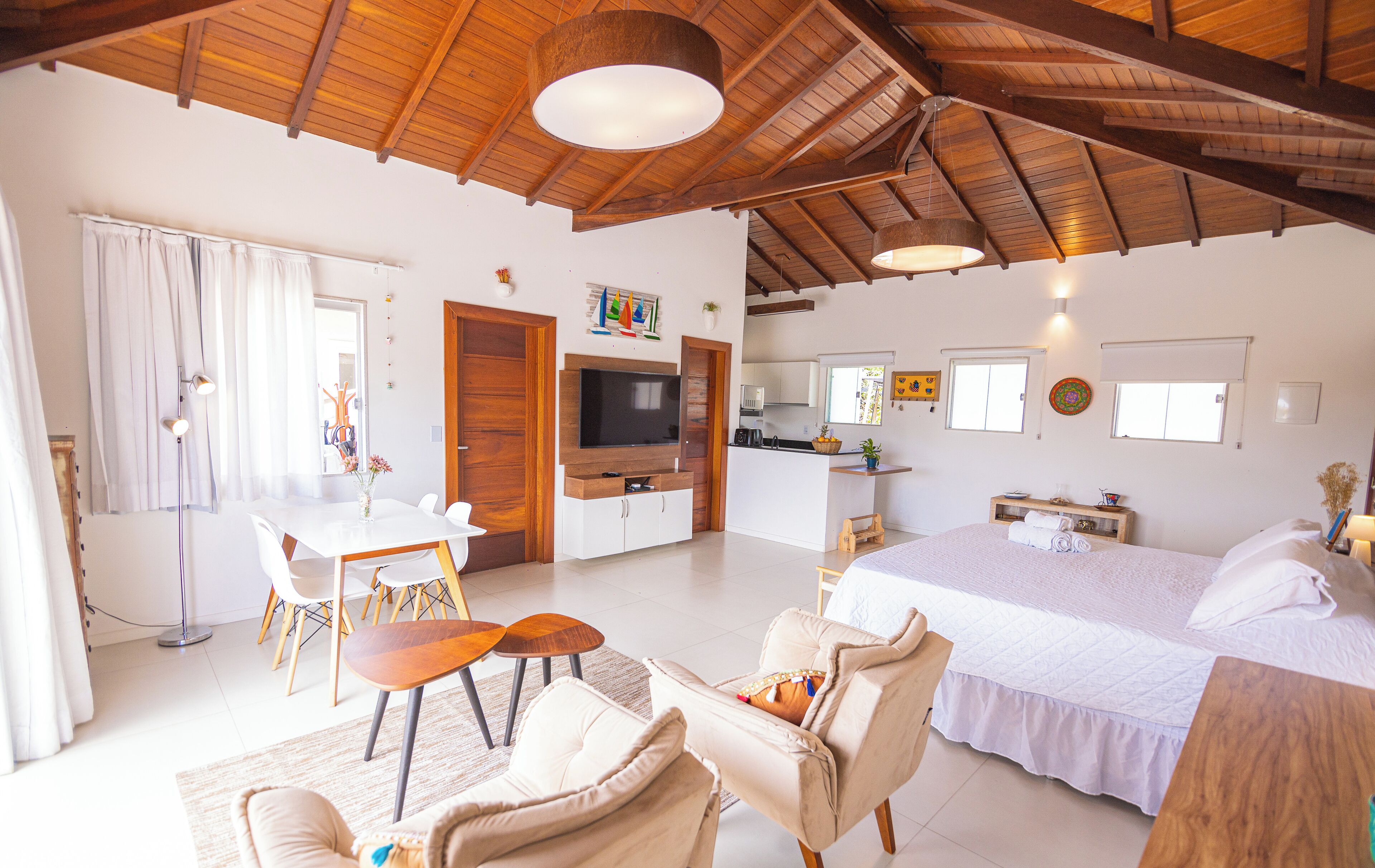 A spacious room with a large bed, a dining area with a table and chairs, a kitchen area, and a ceiling with exposed wooden beams.