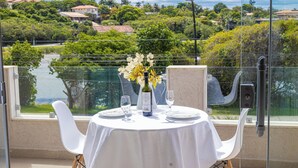 A table set with a bottle of wine, glasses, and a vase of flowers, overlooking a scenic view of a lake and greenery. - Apart Lagoa Buzios- Centro (Búzios)