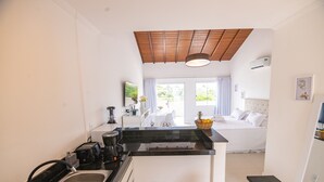 A modern kitchen with a central island, a dining area with a white table and chairs, and a bedroom with a bed and window. - Apart Lagoa Buzios- Centro (Búzios)