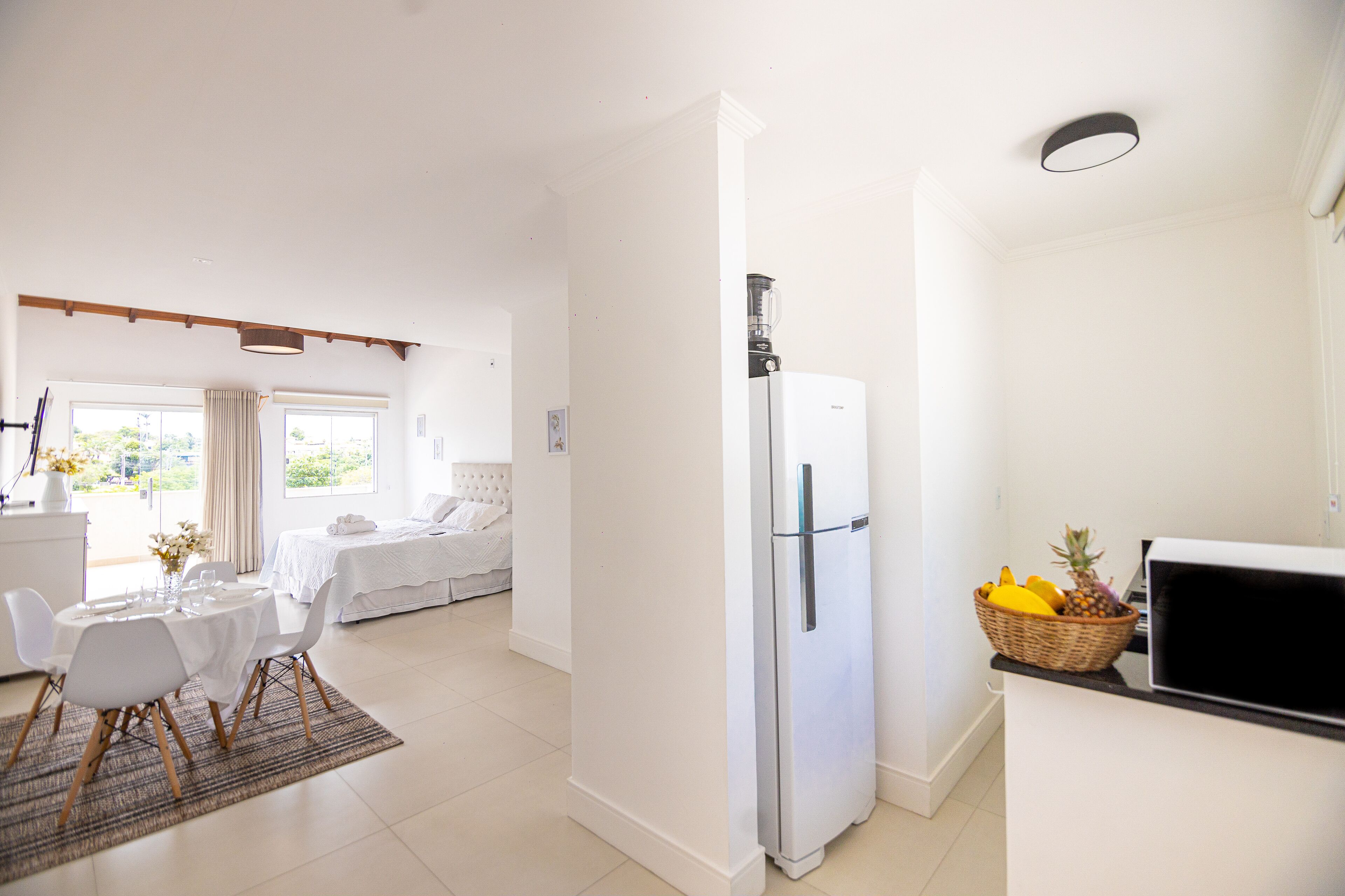 Una cocina moderna con refrigerador, comedor con mesa y sillas, y un dormitorio con cama y cortinas.